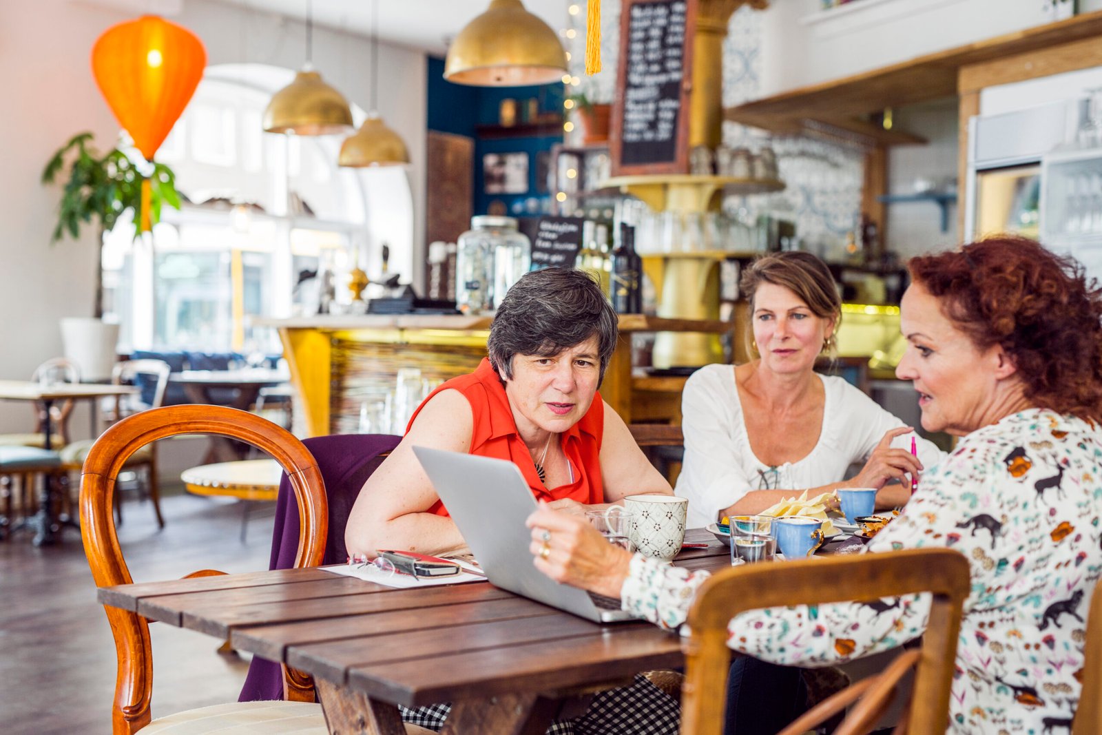 Three small business owners reviewing sponsorship licence requirements on a laptop in a café setting, discussing how to hire overseas staff.