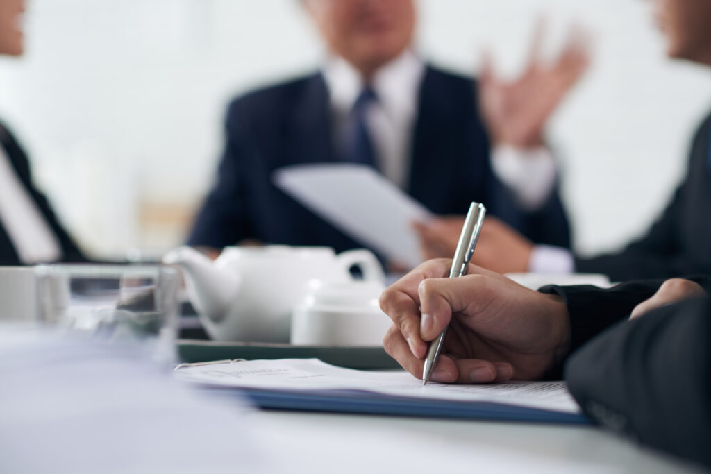 Business professionals reviewing documents and taking notes during a meeting on UK sponsor licence compliance and the Sponsor Management System (SMS).