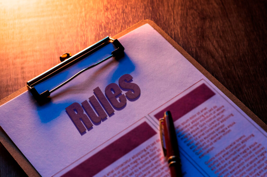 Clipboard with a document titled “Rules” and a pen on a wooden table, symbolising the 2025 sponsor licence rule changes in the UK.