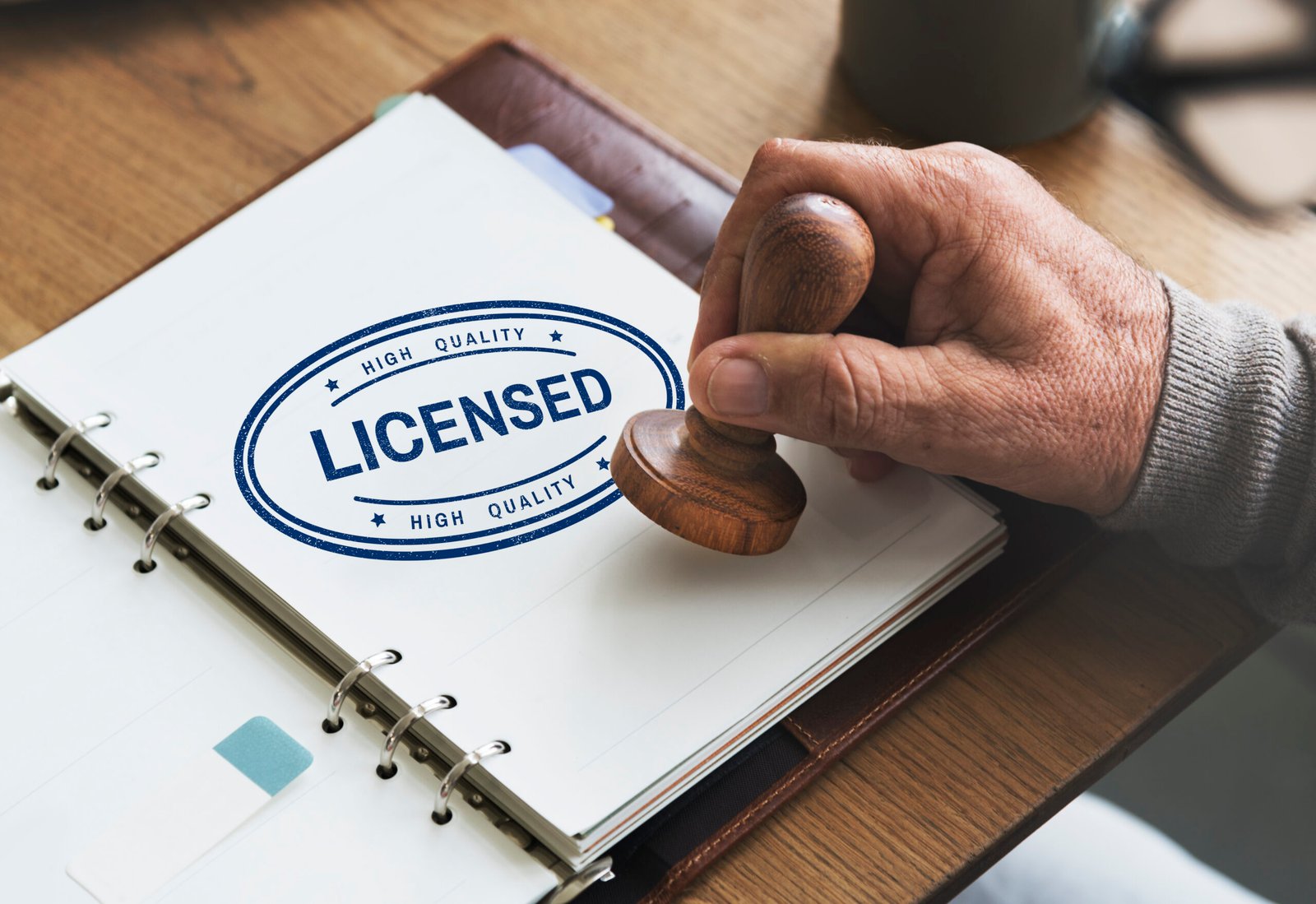 Close-up of a hand stamping a document with a "Licensed" seal, symbolising UK sponsor licence approval.