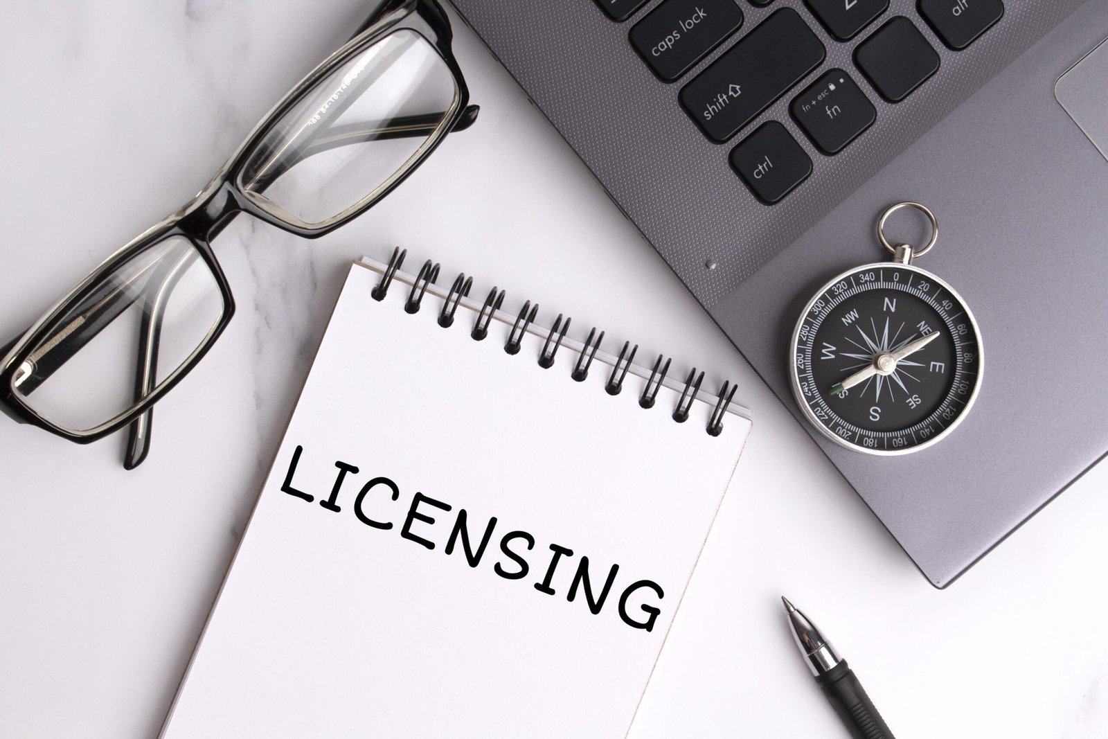 "Business concept showing a notepad with the word 'Licensing', alongside glasses, a laptop, pen, and compass — symbolising direction, compliance, and the strategic benefits of holding a UK sponsor licence for employers."