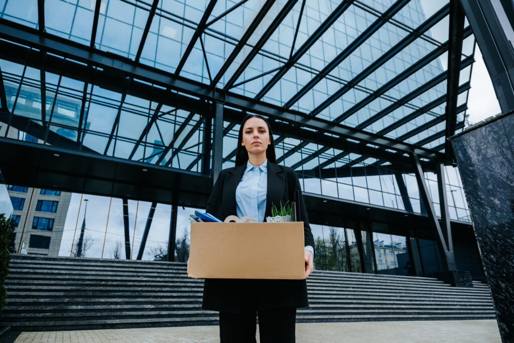 A professional woman carrying a box of belongings after leaving her job, symbolising the early end of sponsored employment in the UK.