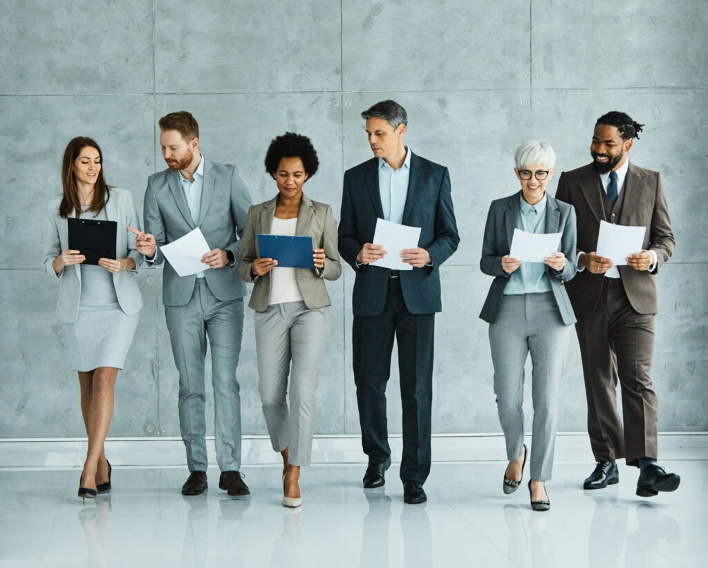 A diverse group of business professionals walking confidently in suits, holding documents, symbolising sponsoring employers obtaining a licence to hire skilled workers in the UK.