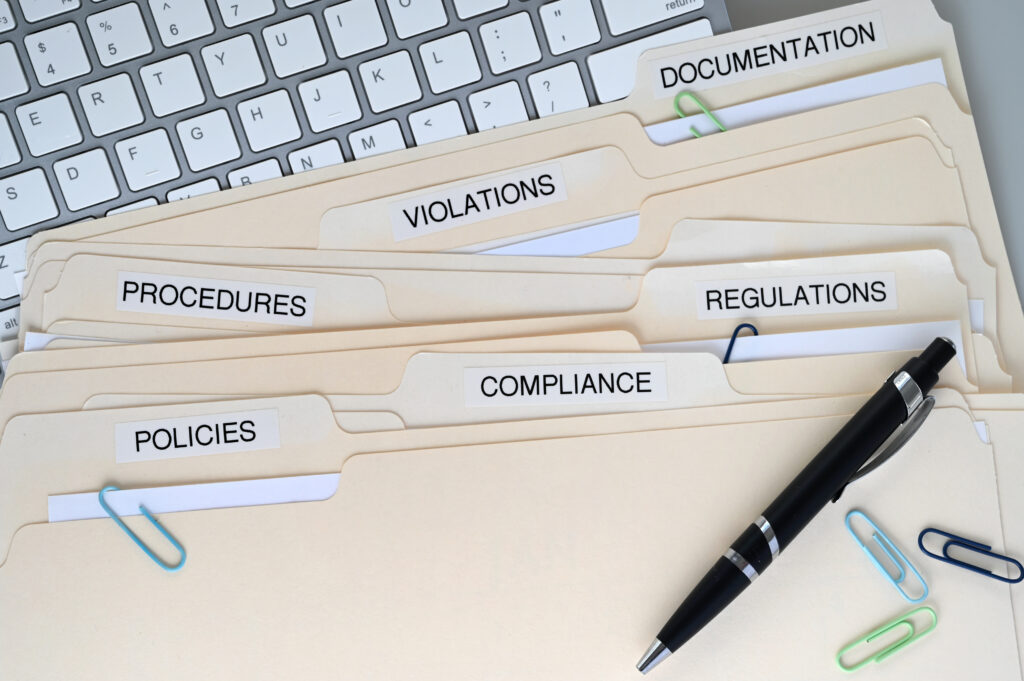 Close-up of compliance folders labelled policies, procedures, regulations, violations, and documentation, symbolising UKVI sponsor licence compliance visit preparation.